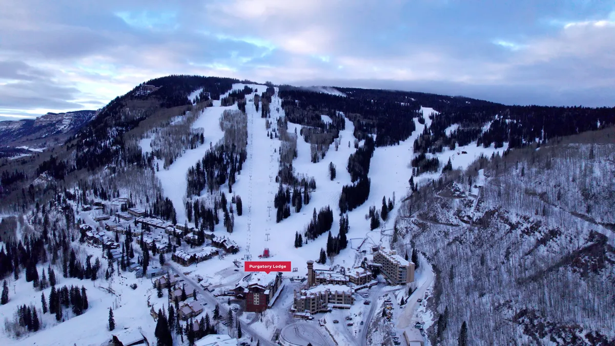 An inviting exterior shot of Purgatory Lodge with ski slopes and a surrounding forest, set against a backdrop of snow and mountains. The image feels cozy yet adventurous, with the lodge offering a point of relaxation after time on the slopes.