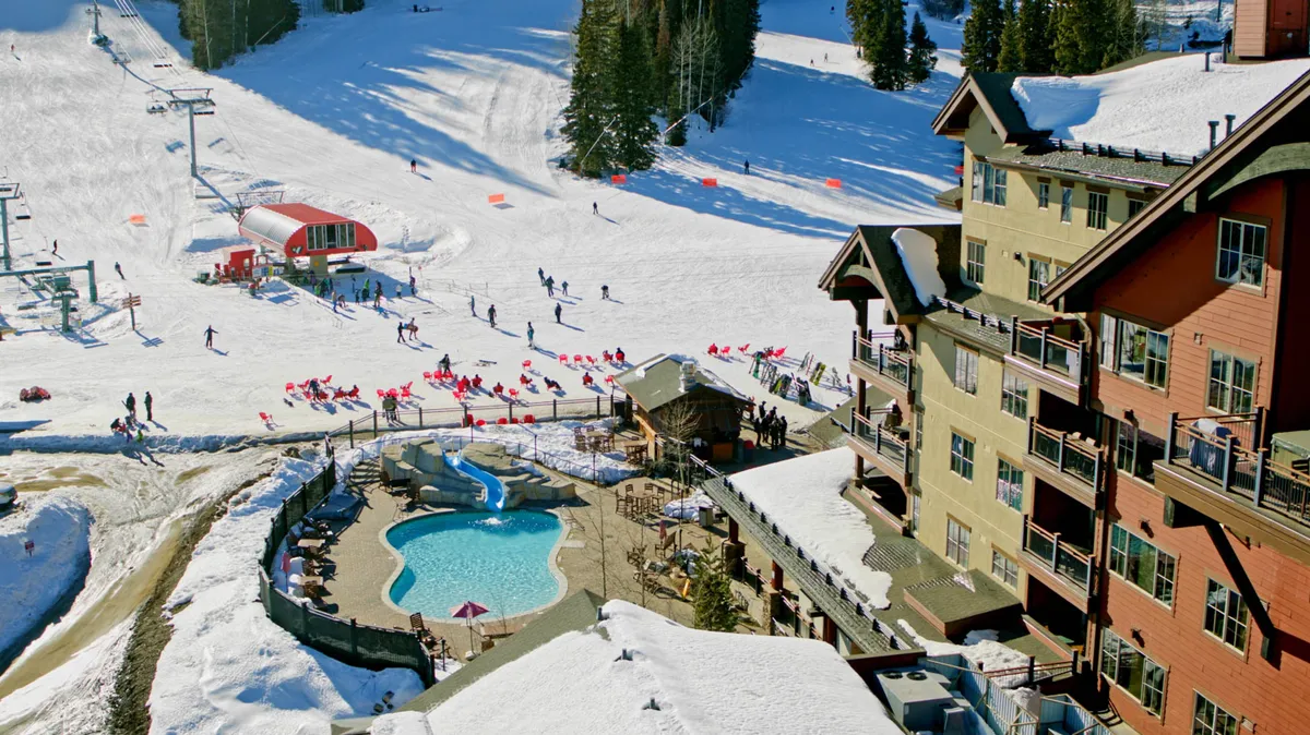 An exterior shot displaying both the ski slopes with skiers in action and a visible pool area next to the building exterior. The scene combines thrilling winter sports activity with relaxation by the pool, encapsulating the dual appeal of adventure and leisure.