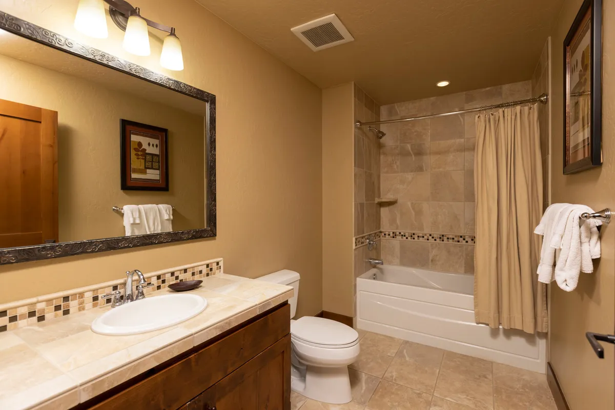 A tranquil bathroom featuring a deep soaking bathtub, a large mirror above a sink, plush towels on a rack, and tasteful wall art. The space is softly lit, conveying a relaxing and refined atmosphere, perfect for unwinding after an active day.