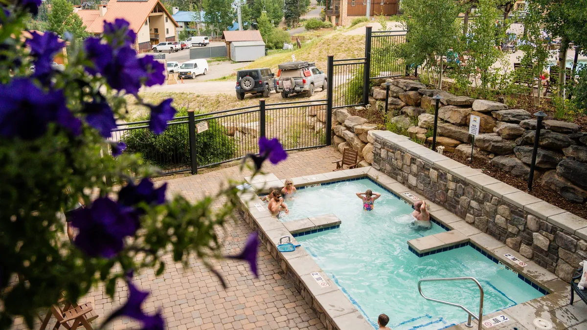 This image captures an inviting outdoor leisure area featuring a hot tub and a swimming pool surrounded by flowering plants and a stone wall. The tranquil setting suggests a resort-style environment where guests can relax, socialize, and enjoy the outdoors, with options for both soaking in the hot tub and swimming in the pool.